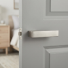 Minimalist internal door handles in an elegant satin nickel finish from the Carlina collection, featuring a hidden rosette on a soft grey paneled door.