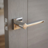Sophisticated square door handles in a mirror-like polished chrome finish from the Ninfea range, mounted on a modern grey wood grain door.