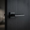 Pea on Square Rosette strong square internal door handles in a bold matt black finish, mounted on a dark textured wood door for a modern look.