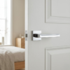 High-shine polished chrome Pea on Square Rosette strong square internal door handles featuring a reflective mirror finish on a classic white paneled door.