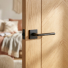 Primula on Square Rosette internal premium door handles in a bold matt black finish, mounted on a natural oak door with a modern chevron pattern.