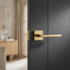 Understated square door handles in a brilliant PVD gold finish from the Pyrola range, mounted on a sophisticated dark charcoal interior door.