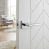 High-shine polished chrome Pyrola on Square Rosette understated square door handles featuring a reflective finish on a white chevron-patterned door.