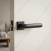 Stella on Square Rosette sophisticated square door handles in a bold matt black finish, mounted on a white door with a modern diagonal wood grain pattern.