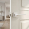 Contemporary matt white Yuka on Square Rosette sleek square internal door handles installed on a bright, off-white paneled door.