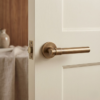 Bellisa on Round Rosette contemporary internal door handles in a warm antique patina finish, installed on a classic cream-colored paneled door.