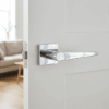Arnica on Square Rosette in polished chrome, a reflective premium internal door handle fitted to a modern white door.