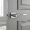 Bergenia on Square Rosette in polished chrome, a reflective elegant door handle for internal doors installed on a grey panelled door.