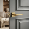Minimalist square door handles with the Funkia lever on a square rosette in PVD gold, displayed on a grey internal door for an elegant modern finish.