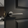Sleek internal door handles in a graphite finish, featuring the Kerria design on a round rosette fitted to a dark modern door.