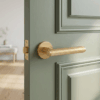 Sleek internal door handles in a matt gold finish, highlighting the Kerria handle on a round rosette installed on a green panelled door.