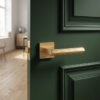 Bold square internal door handles in a matt gold finish, featuring the Larice on Square Rosette fitted to a deep green panelled door for a striking contemporary interior.