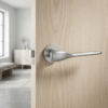 Satin chrome Orchide on Round Rosette on a pale wood door, offering elegant curved door handles in a sleek brushed finish.