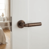 Ficaria on Round Rosette in burnt umber, showcasing elegant brass door handles with a warm, vintage tone on a white door.